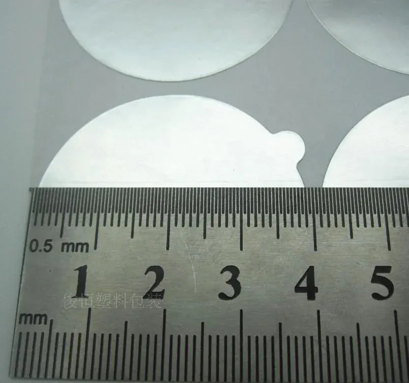 Close-up of round aluminum seal stickers measured with ruler, about 0.5 mm