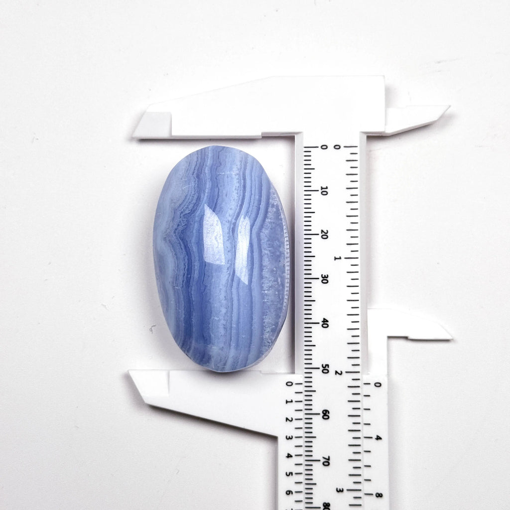 Blue lace agate palm stone, oval tumbled gem with blue banding beside ruler