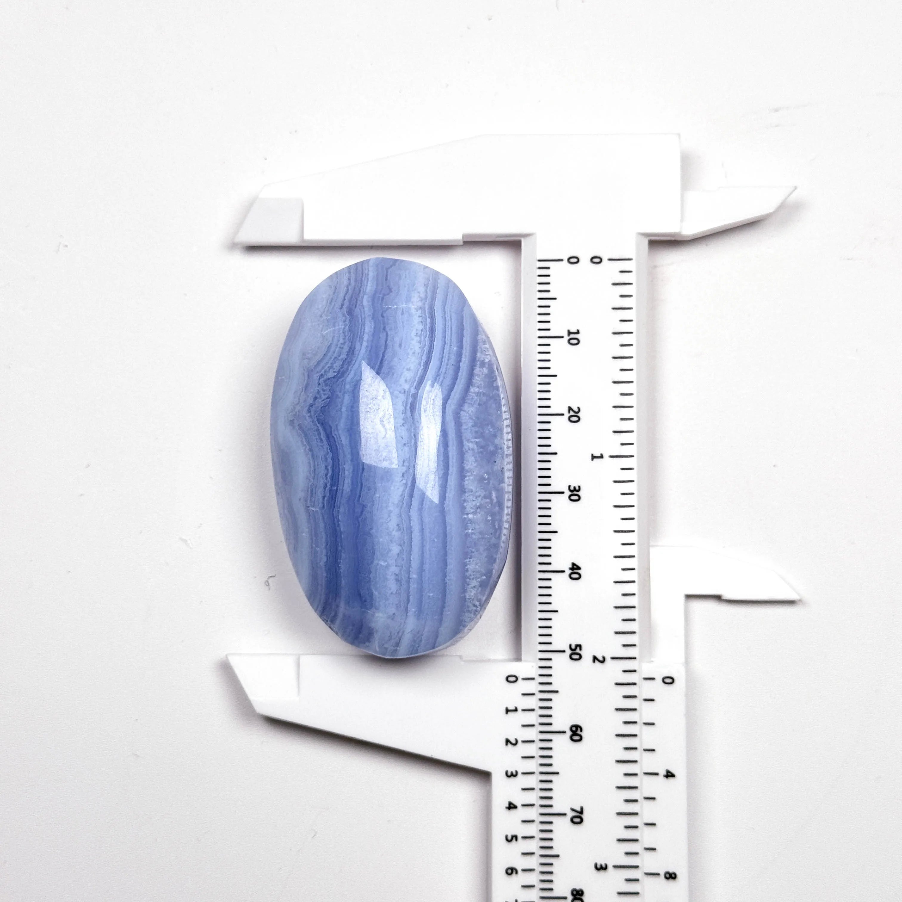 Blue lace agate palm stone, oval tumbled gem with blue banding beside ruler