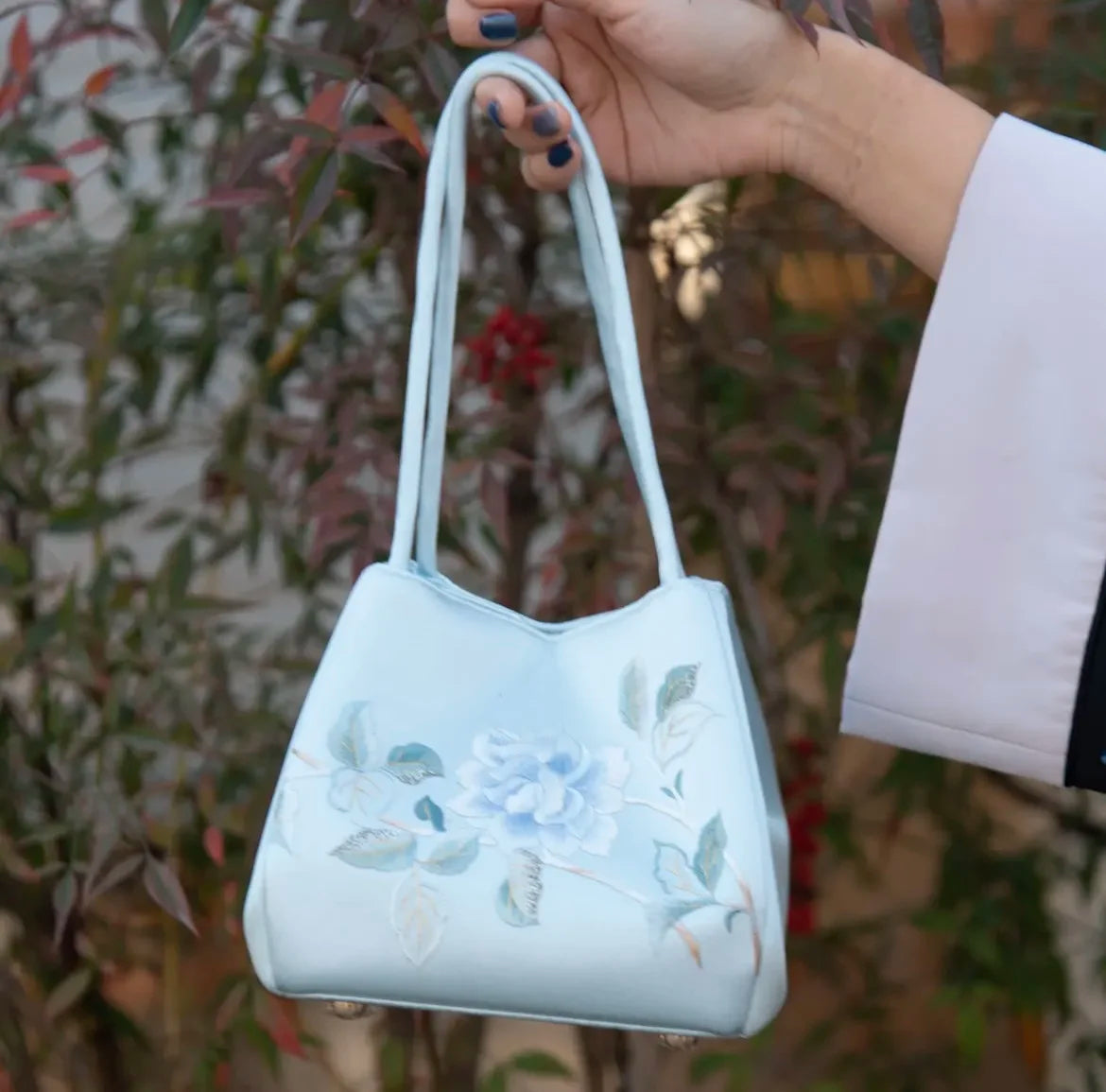 Light blue designer handbag with classic floral Su embroidery, elegant daily tote style, held in hand.