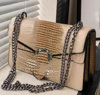 Beige crocodile-pattern trunk crossbody bag with chain strap and metallic clasp for women.