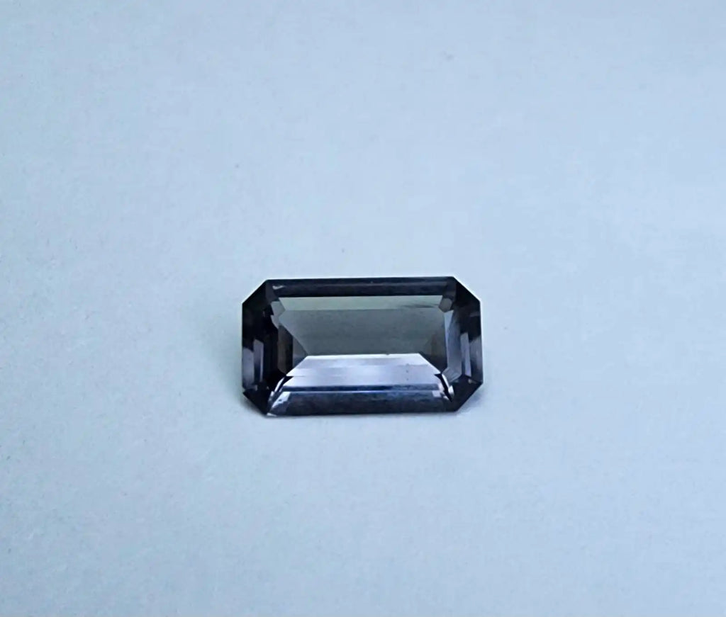 Dark gray emerald-cut spinel gemstone with reflective step facets