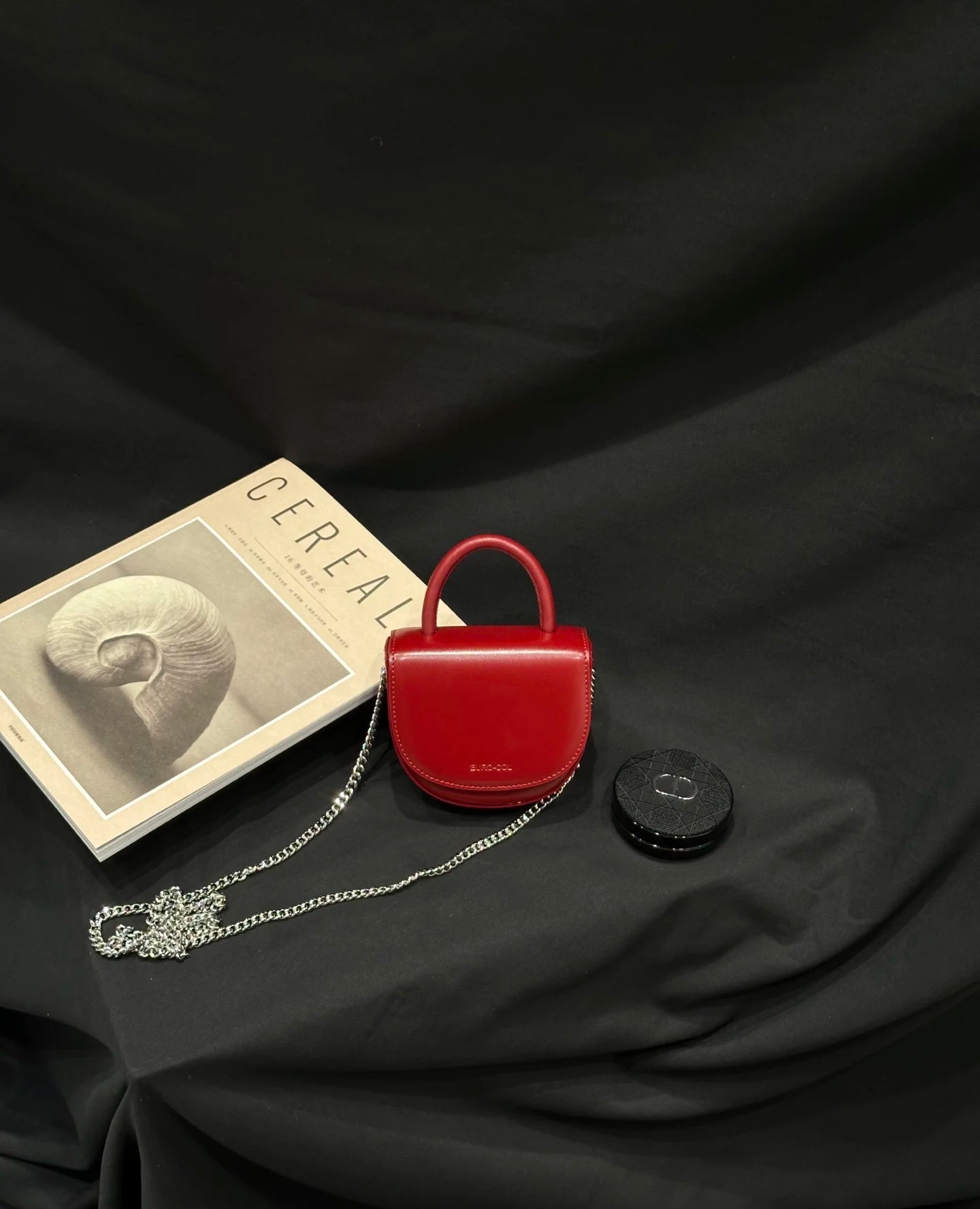 Small red cowhide leather evening clutch, saddle shape, top handle, and silver chain strap for designer handbags.