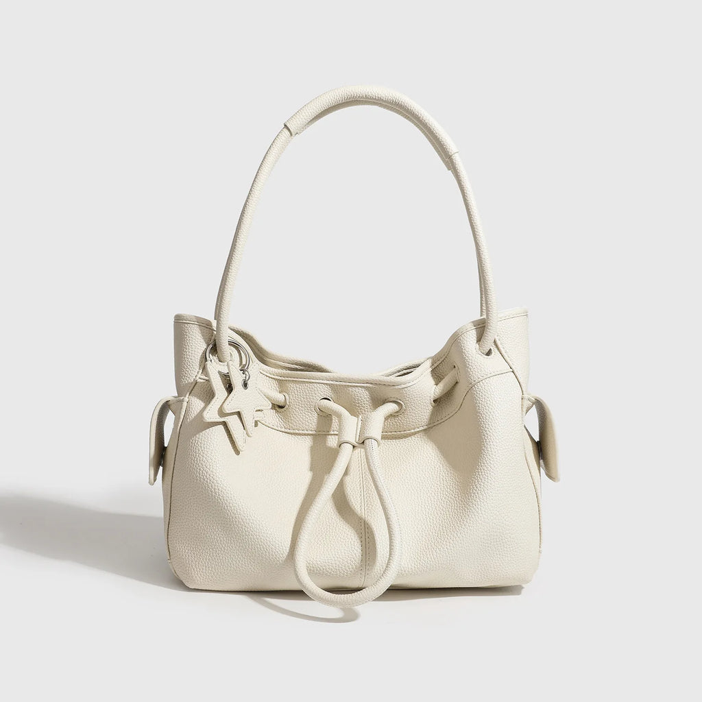 Off-white pebble-grain leather shoulder bag with drawstring closure, dual straps, and star charm. Minimalist aesthetic.