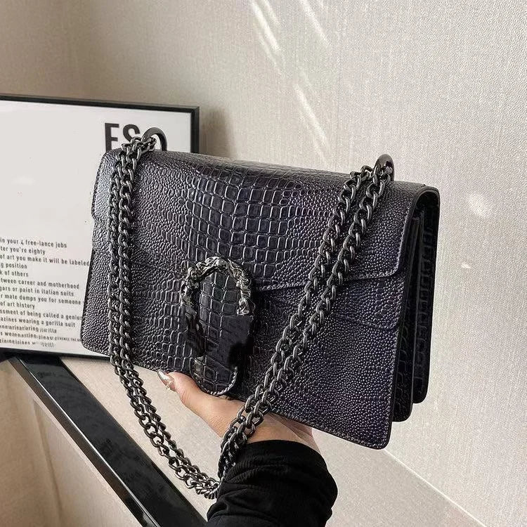 Black crocodile-pattern luxury crossbody trunk bag with metallic chain strap and ornate horseshoe-style clasp.