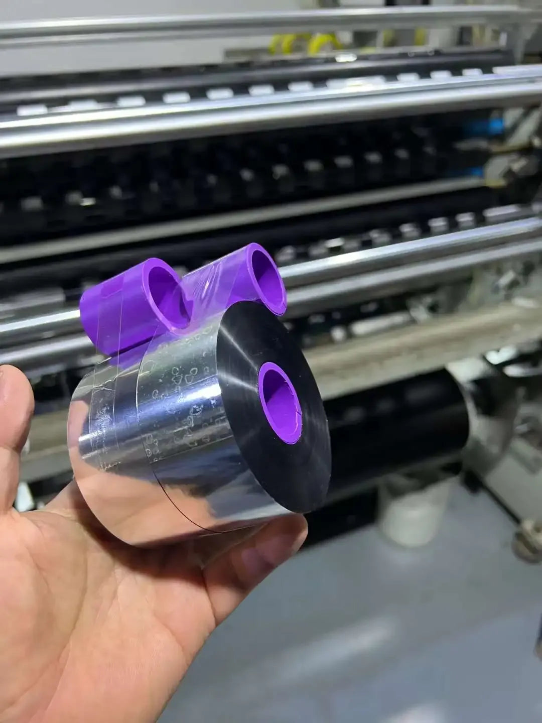 Hand holding black wax-resin thermal transfer ribbon roll with purple center