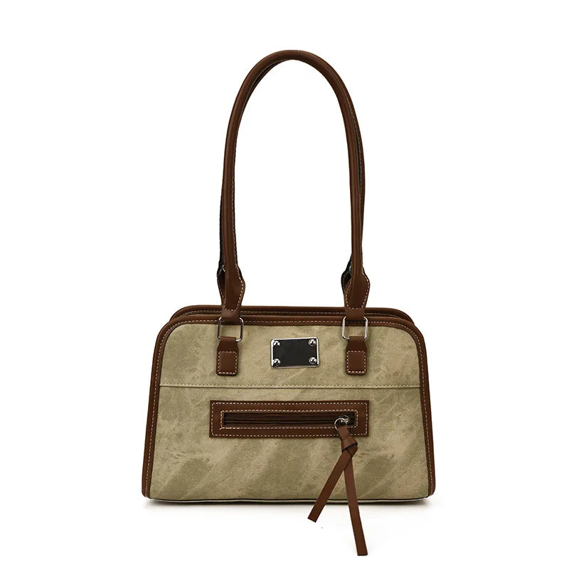 Khaki suede and brown leather trunk tote bag with shoulder straps, front zipper pocket, and metallic rectangular tag.