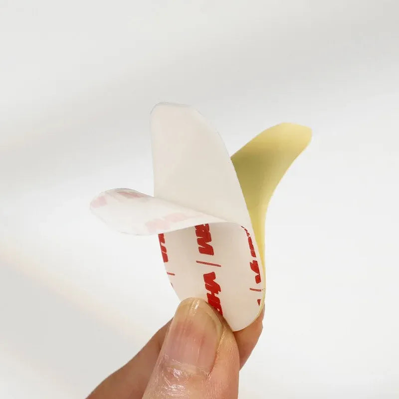 Hand holding a transparent white double-sided acrylic foam tape pad, round die-cut