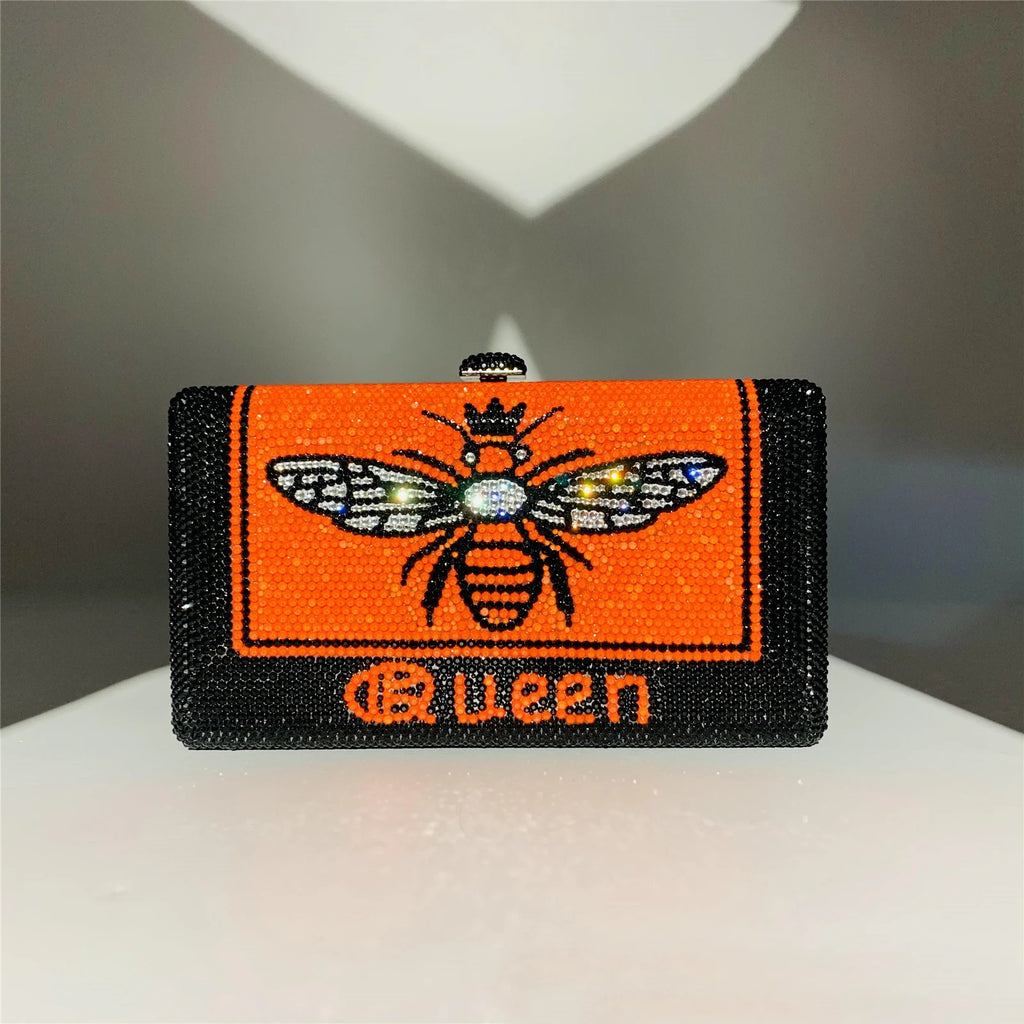 Black and orange rhinestone hard shell evening clutch with bee graphic and "Queen" text. Designer handbag style.