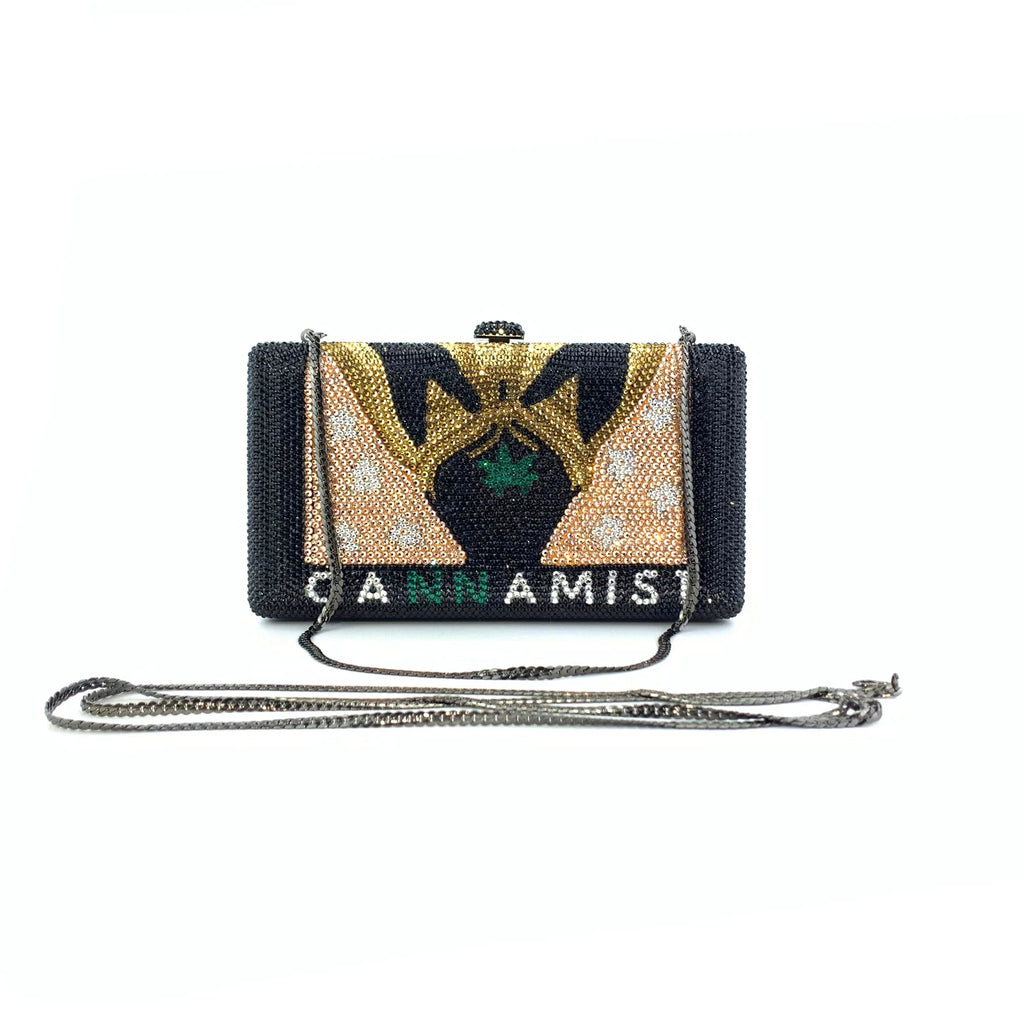 Black crystal treasure chest clutch with gold and green inlaid design, chain strap, and "CANNAMIST" lettering.
