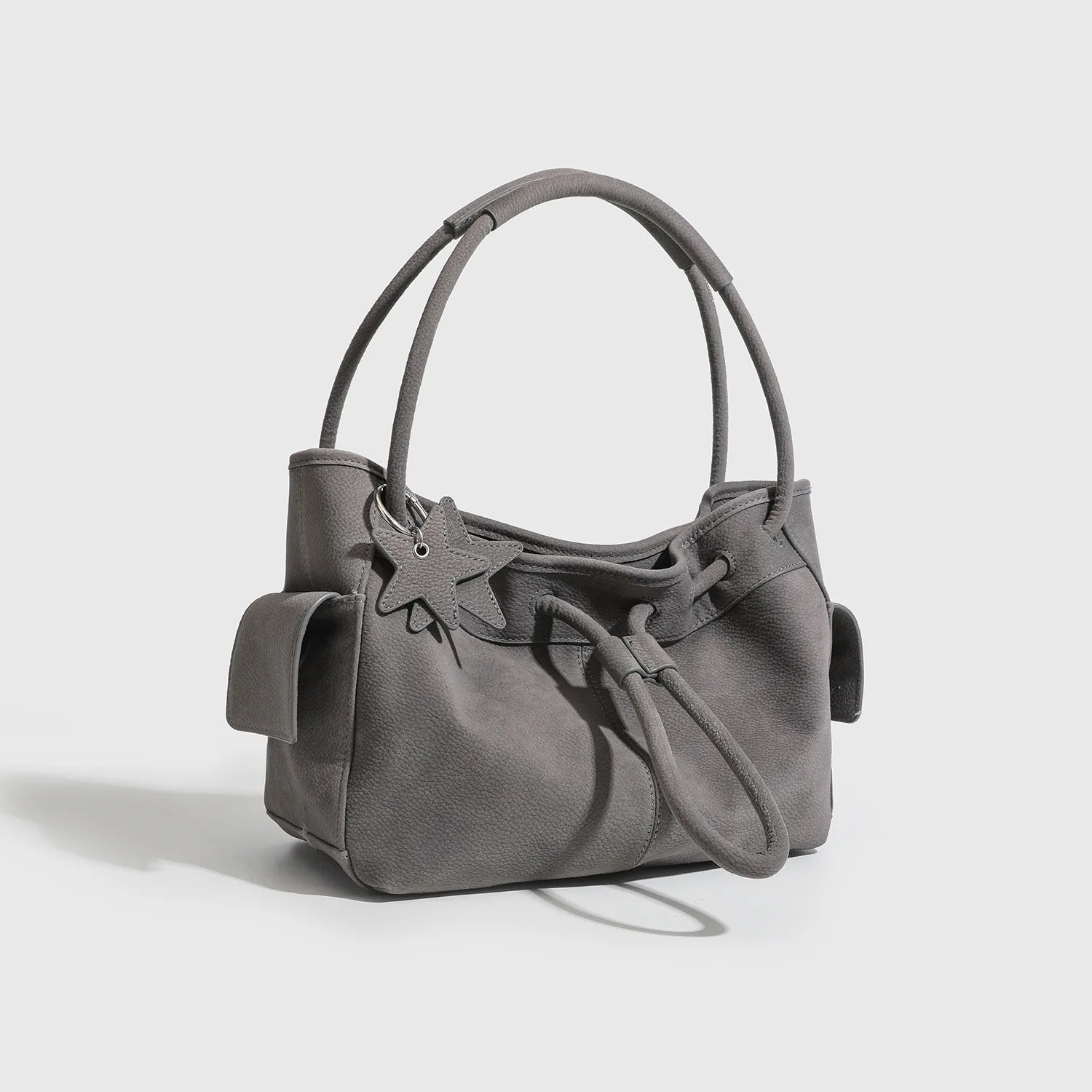 Grey designer shoulder bag with double straps, star charm, drawstring closure, and large side pockets for commuting.