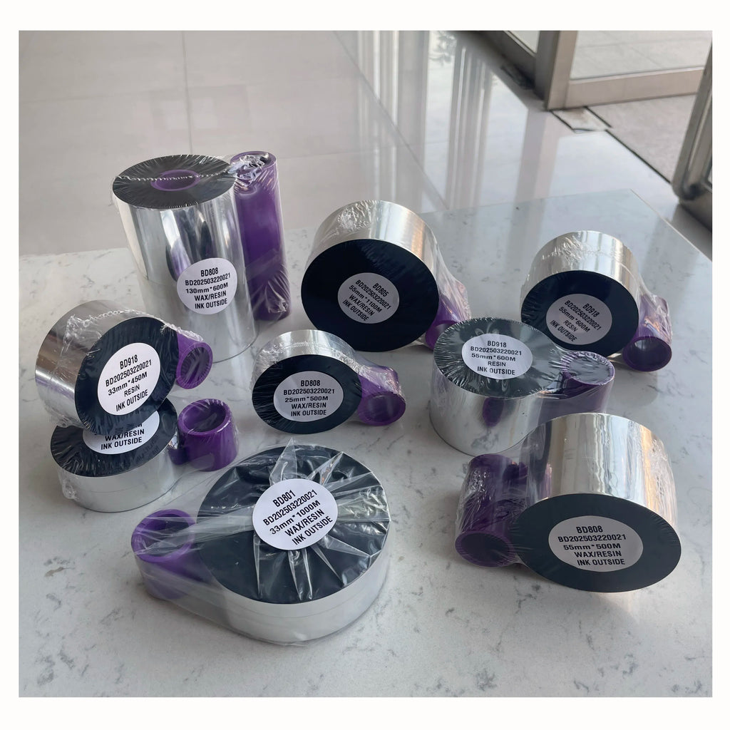 Assorted thermal TTO ribbon rolls, silver spools with dark cores and purple packaging.