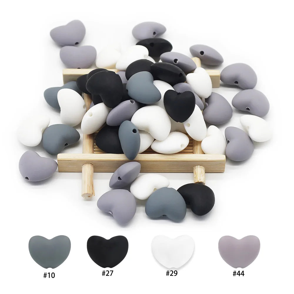 Black, white, and grey silicone heart-shaped beads for baby teething toys on a wooden rack.