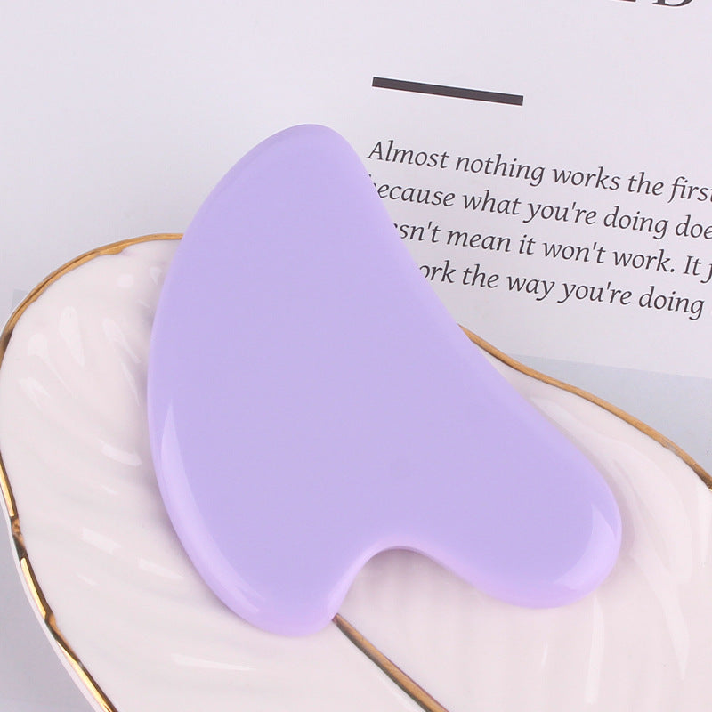 Smooth, heart-shaped light purple resin gua sha facial massage tool resting on a white decorative dish.