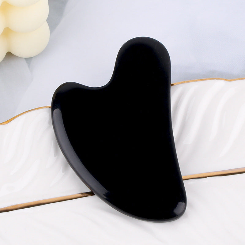 Glossy black, heart-shaped resin gua sha facial massage tool resting on a white surface.