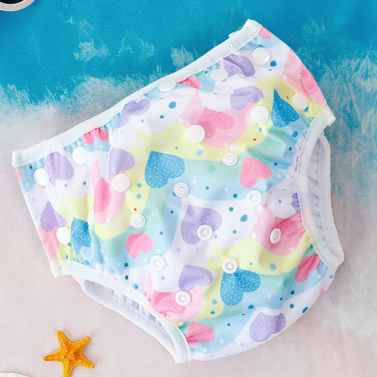 Reusable baby swim diaper with adjustable snaps, featuring a colorful rainbow and heart print on a blue background.