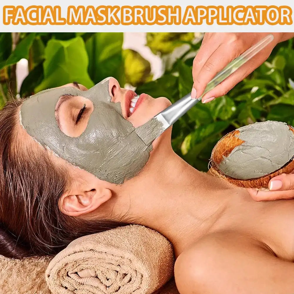A transparent handled brush applying a gray clay facial mask to a woman's face from a coconut shell bowl.