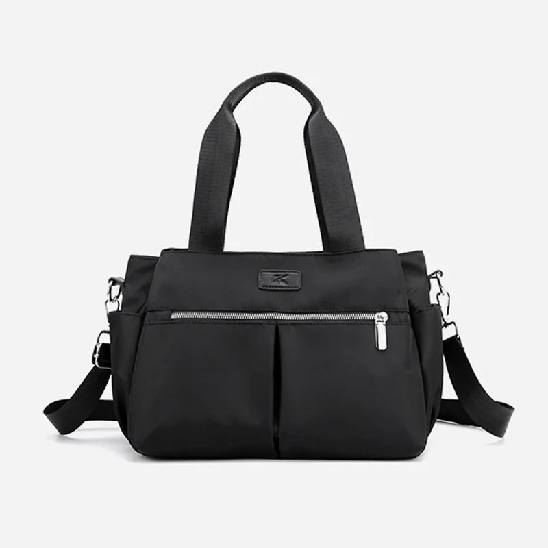 Black minimalist canvas designer handbag with top handles, silver zipper, and detachable shoulder strap.