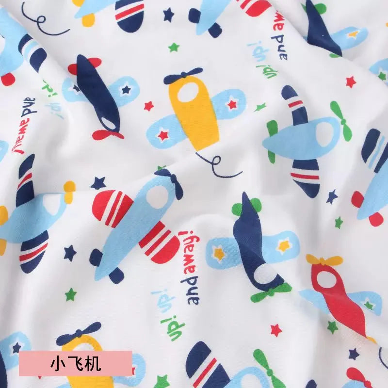 White knit jersey fabric with a colorful print of blue, yellow, and red toy airplanes and stars, soft cotton texture.