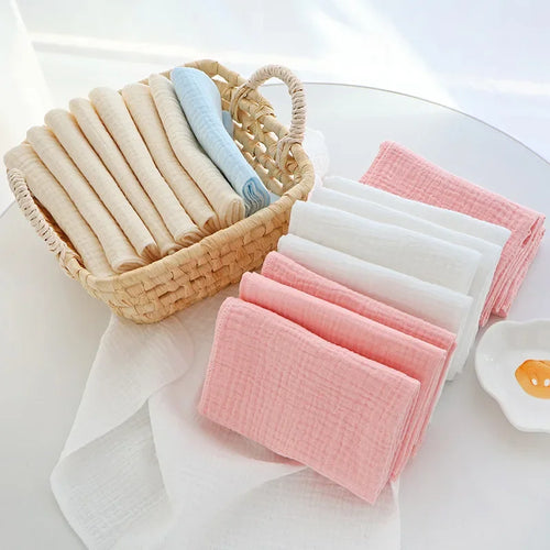 Set of soft muslin baby care cloths in pastel pink, white, and blue, organized in a woven basket.