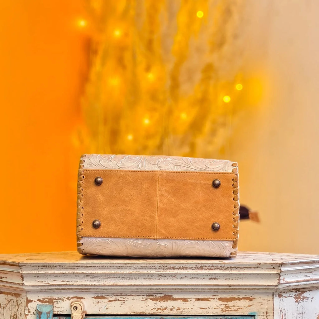 Tan and white hand-tooled floral leather mini duffel bag with protective metal feet and whipstitch detailing.