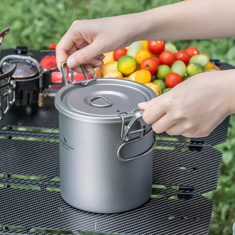 Titanium rice cooker pot with open lid, hands serving food on camping table