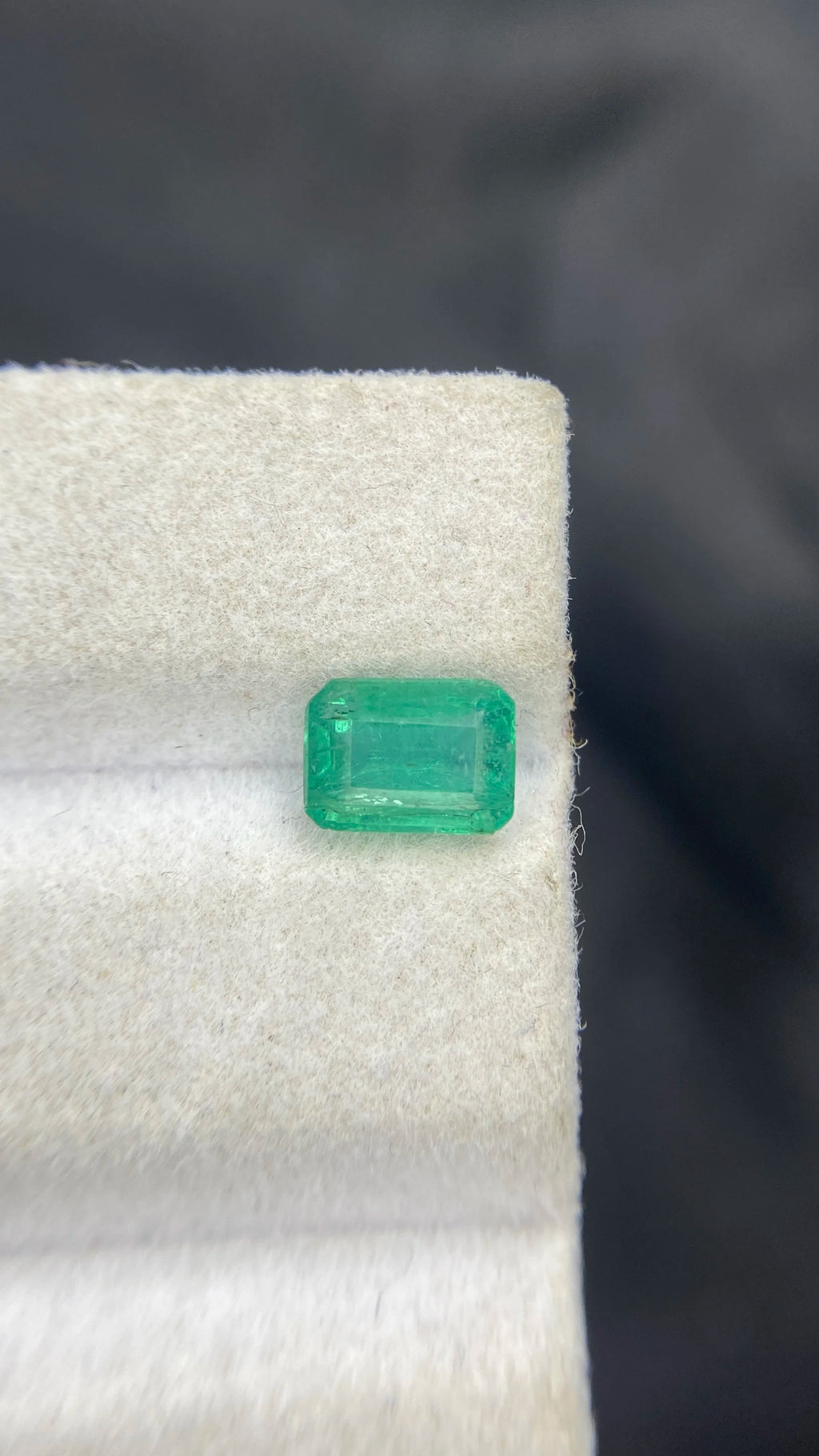 Loose emerald-cut green gemstone, front view on white felt pad