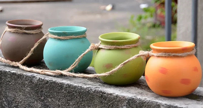 Set of ceramic hanging flowerpots on a ledge: brown, teal, green, and orange