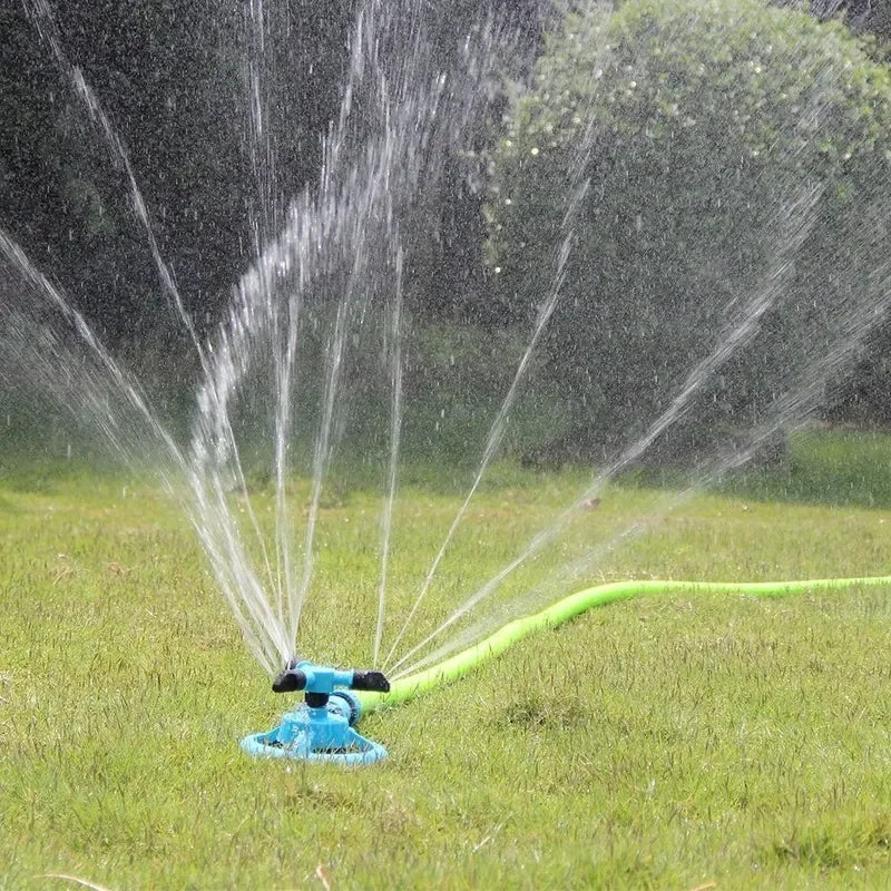 Rotary lawn sprinkler spraying fine water mist across the lawn from a round teal base.