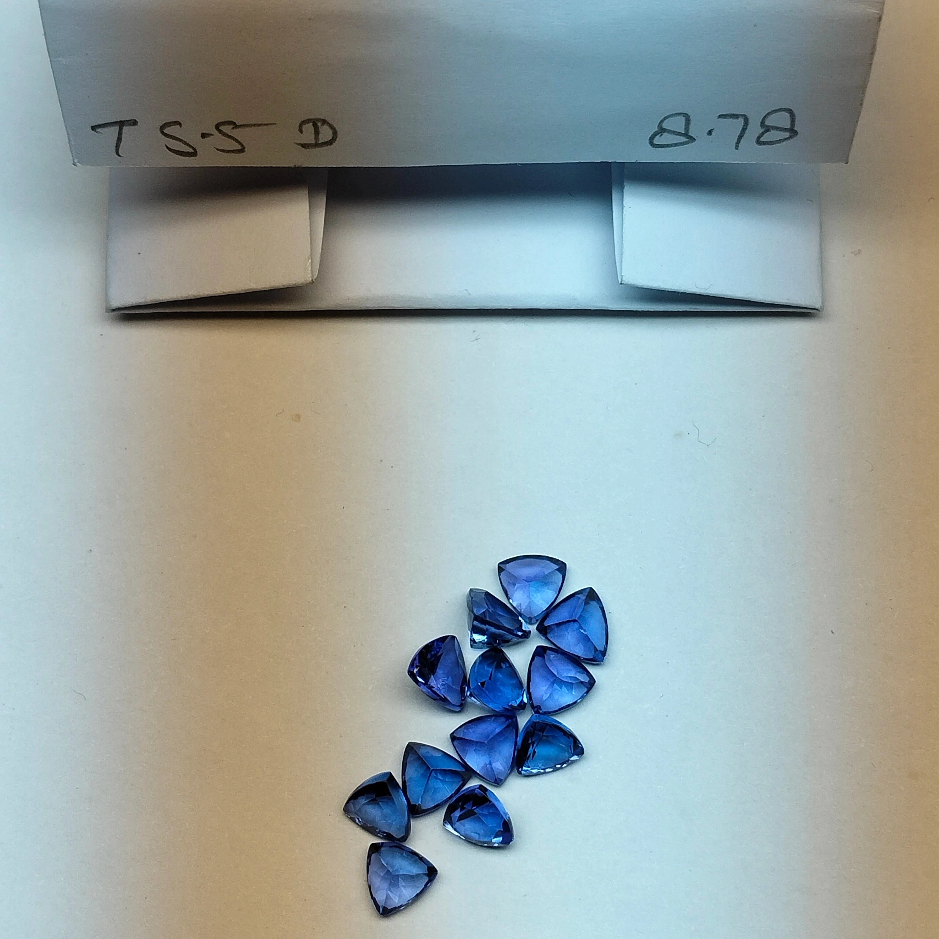 Loose blue trillion-cut gemstones placed beside a storage box