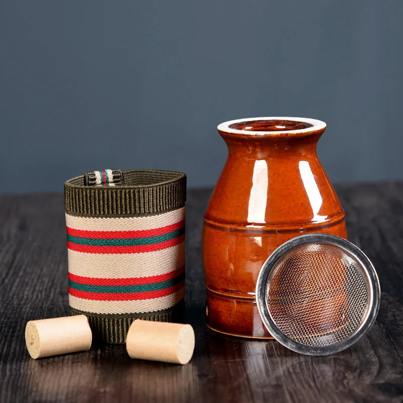 Brown ceramic moxibustion burner, a striped fabric sleeve, two wooden stoppers, and a metal mesh filter on a table.