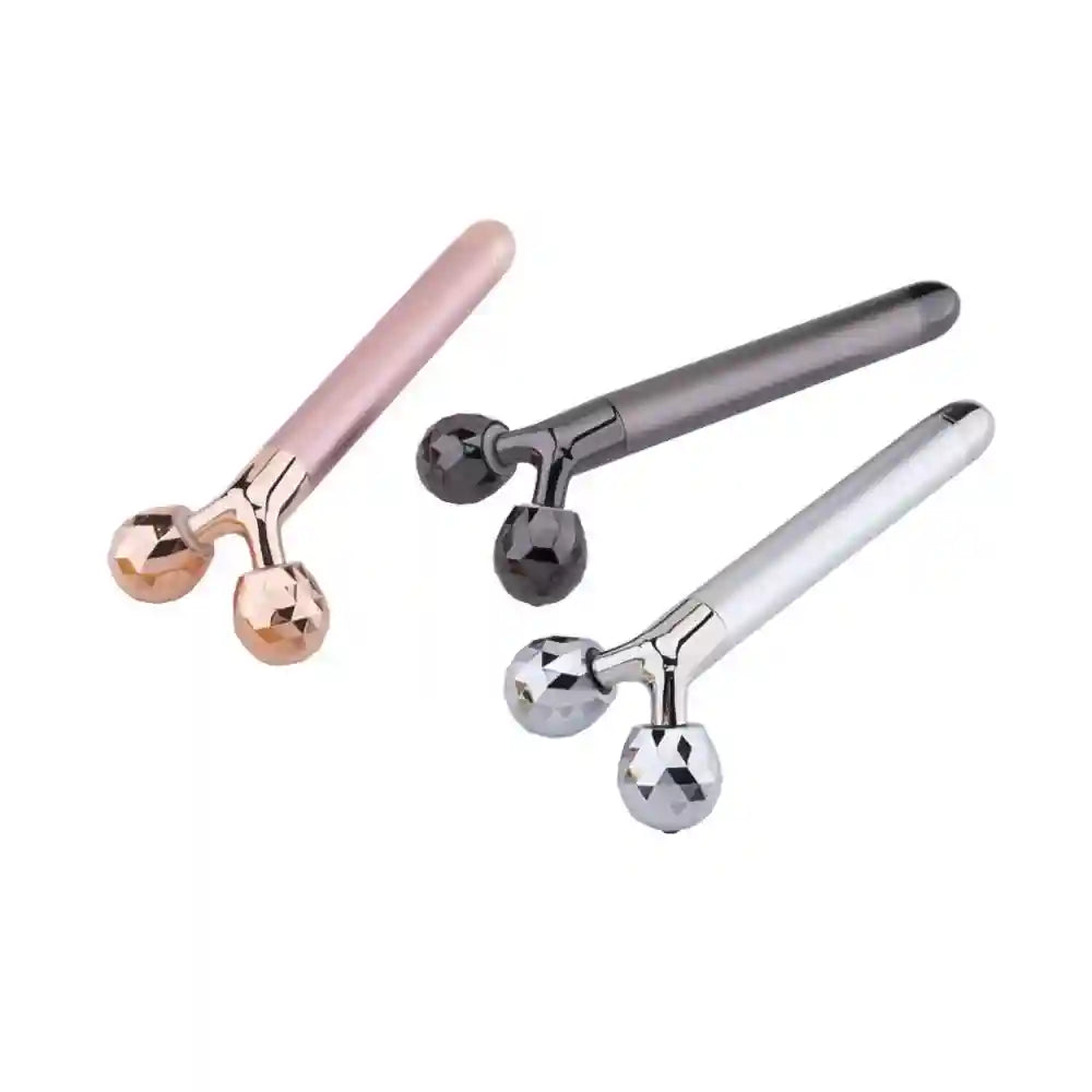 Three facial massagers in rose gold, gunmetal, and silver with Y-shaped heads featuring dual faceted rotating spheres.