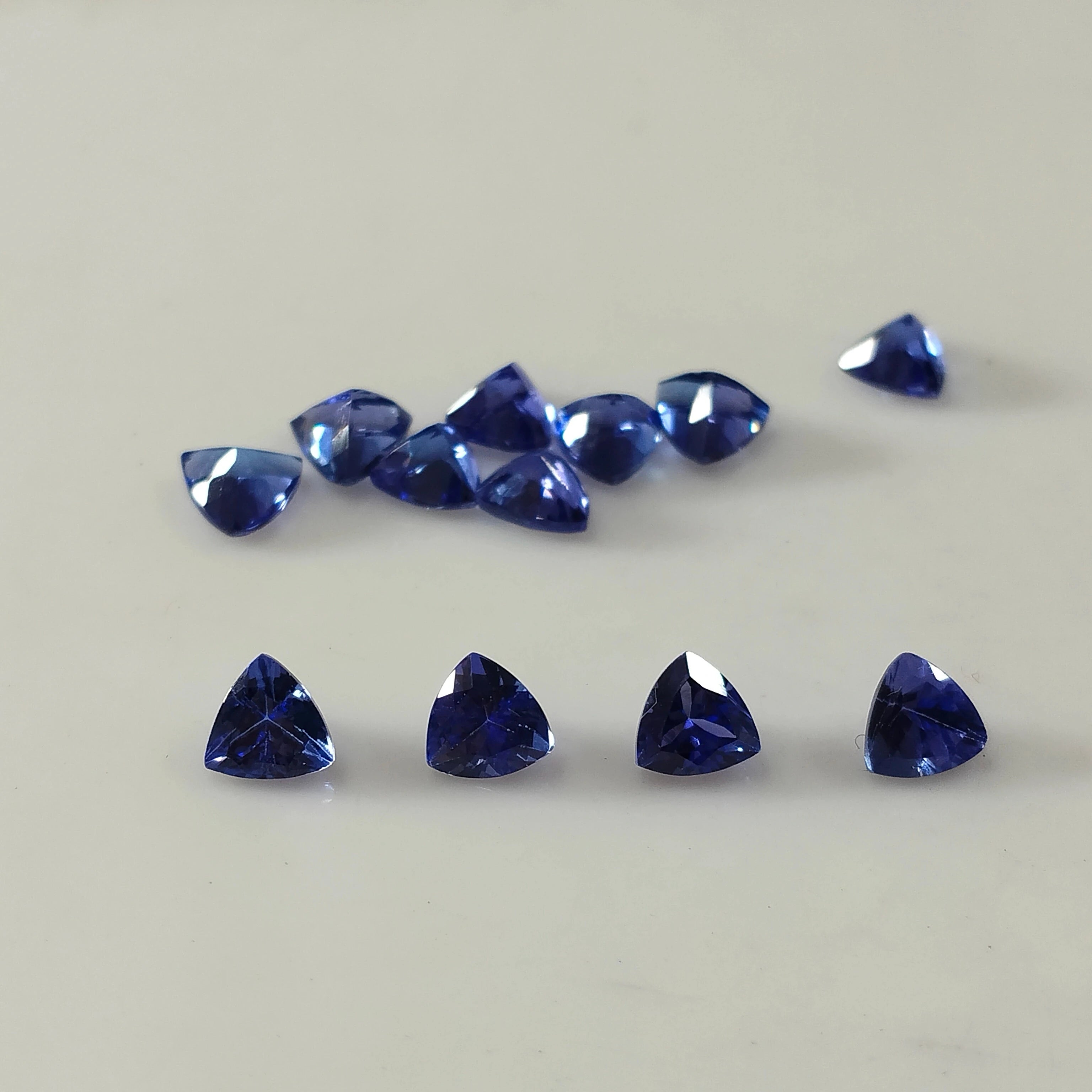 Loose blue trillion-cut gemstones arranged in a line, with extra loose stones