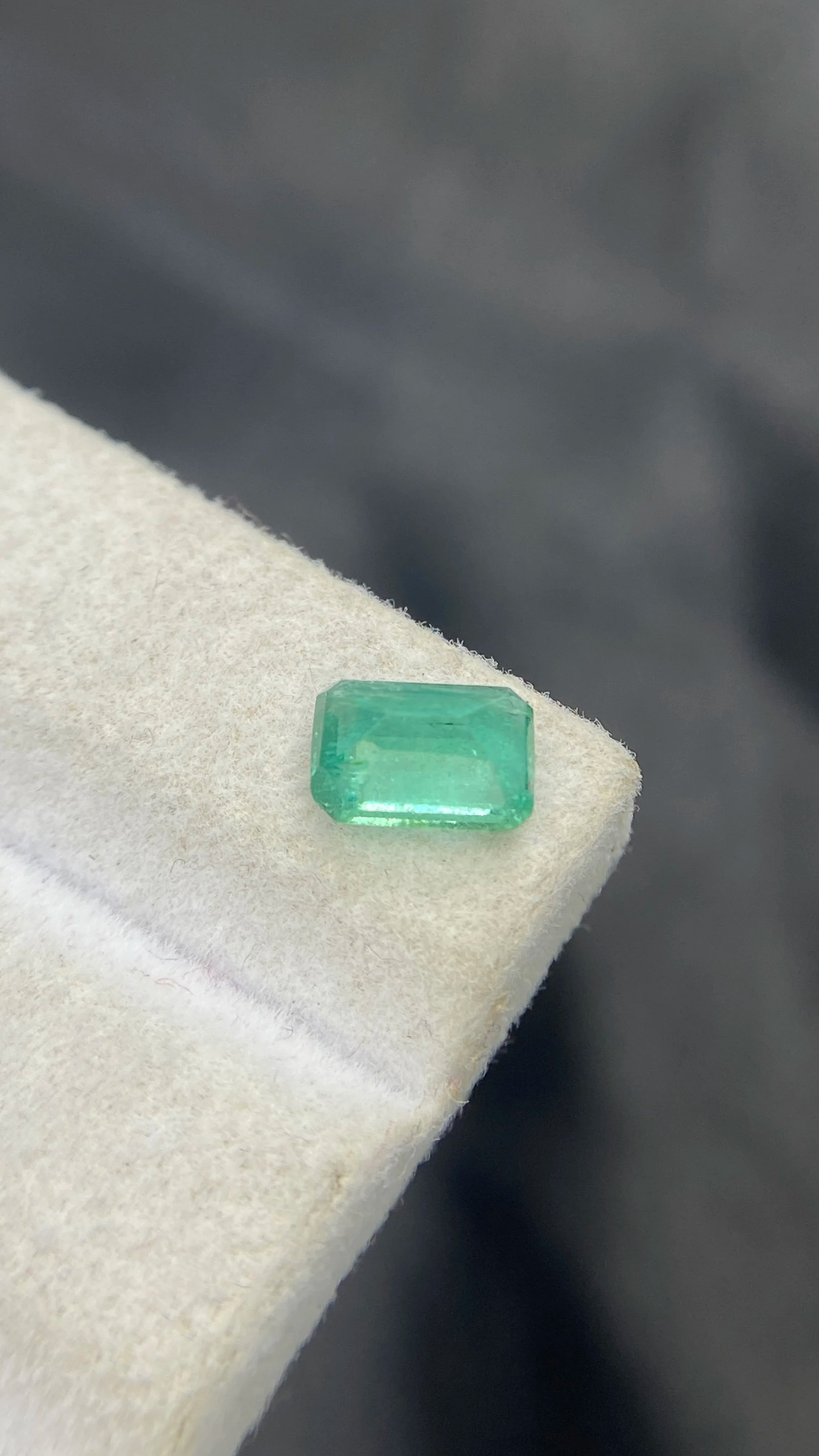 Loose emerald-cut green gemstone, slight side angle on white felt