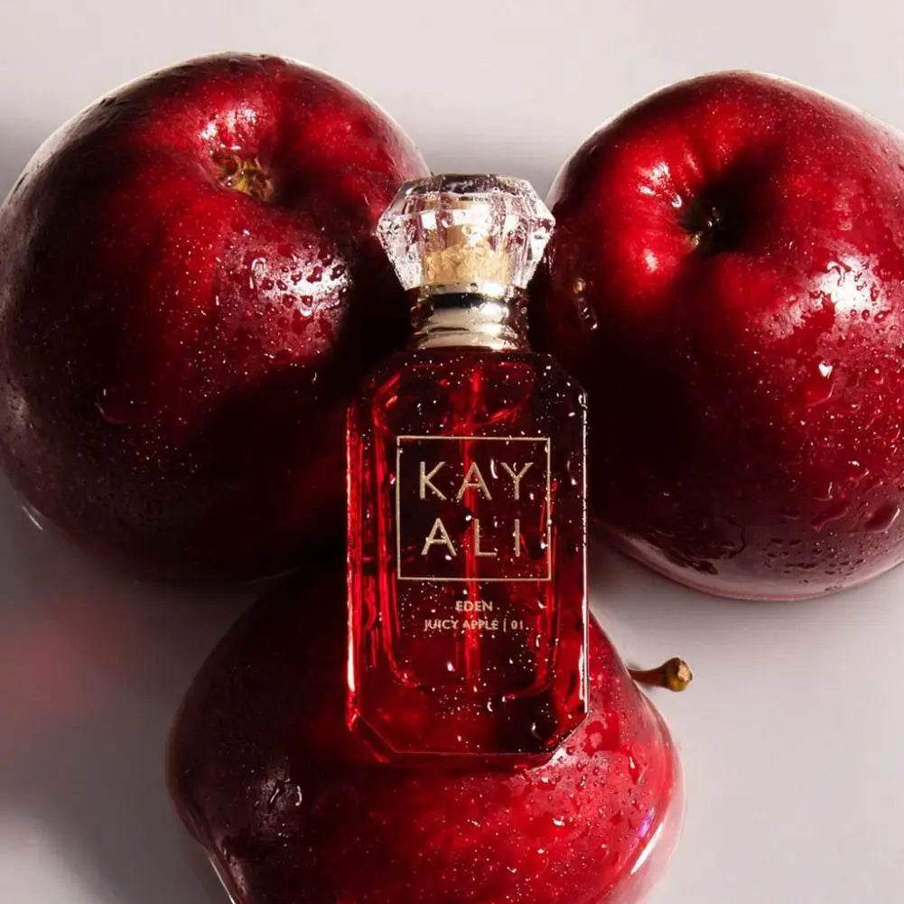 Kayali Eden Juicy Apple EDP 100ml: luxury floral fruity perfume in a glass bottle with diamond-cut cap among red apples.