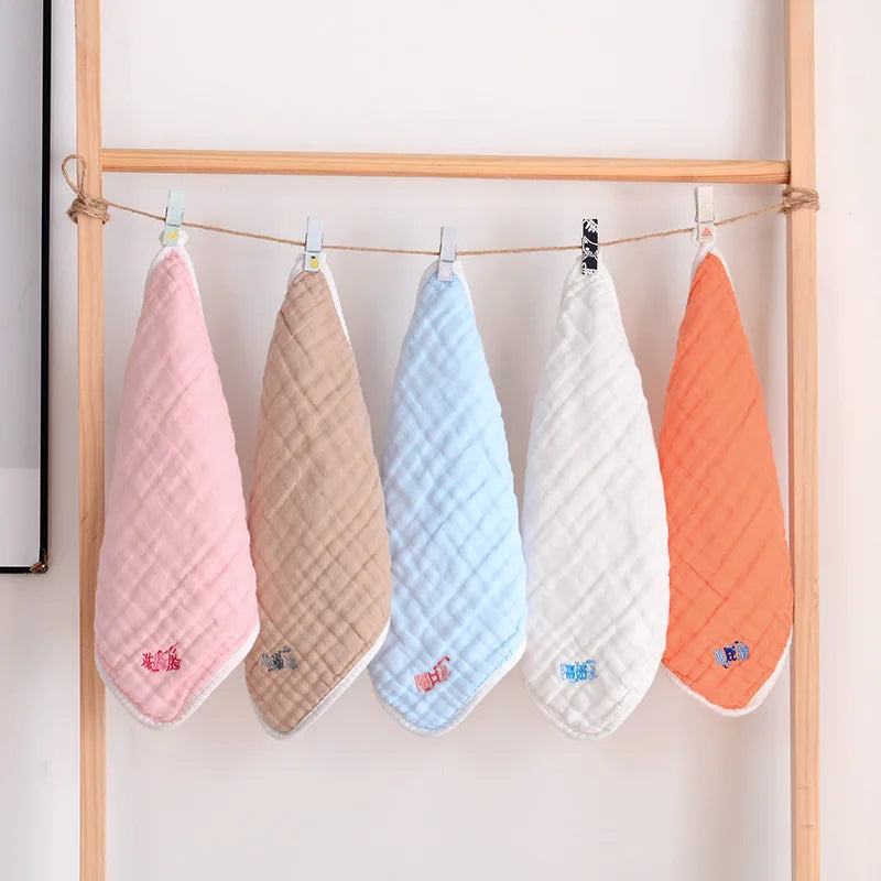 Set of 5 soft muslin baby care washcloths in pastel colors, quilted fabric, hanging on a line.