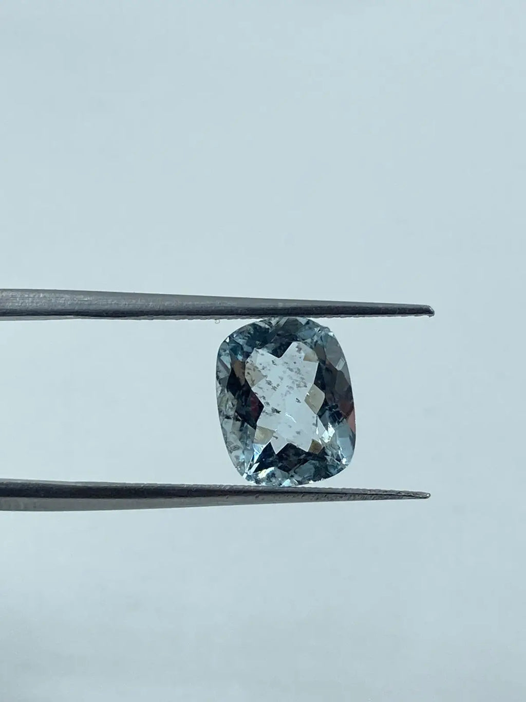 Loose cushion-cut aquamarine gemstone, sky blue, centered between tweezers, side view