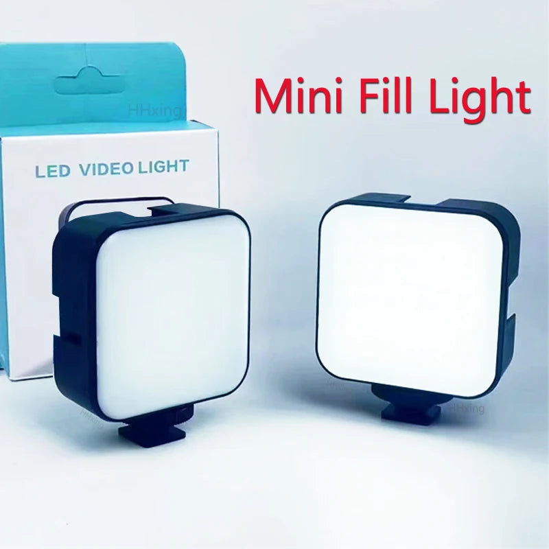 Two square, black mini LED video lights with white diffuser panels and mounting bases, shown next to their retail box.