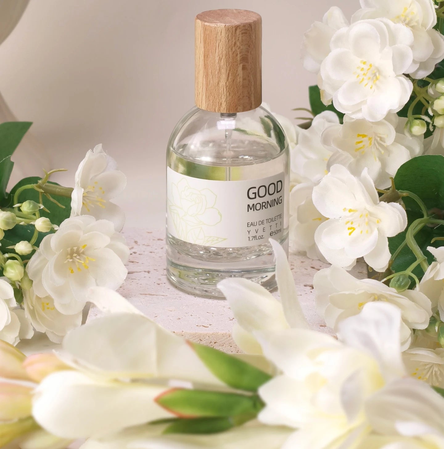 Clear glass perfume bottle with wooden cap, Good Morning label, surrounded by elegant white gardenia flowers.