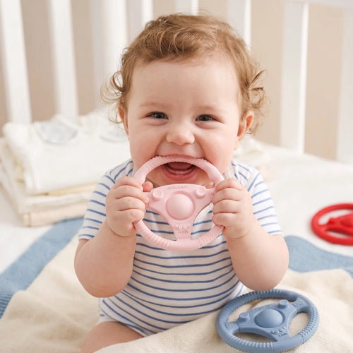Baby chewing on a pink silicone steering wheel baby teething toy for pain relief.