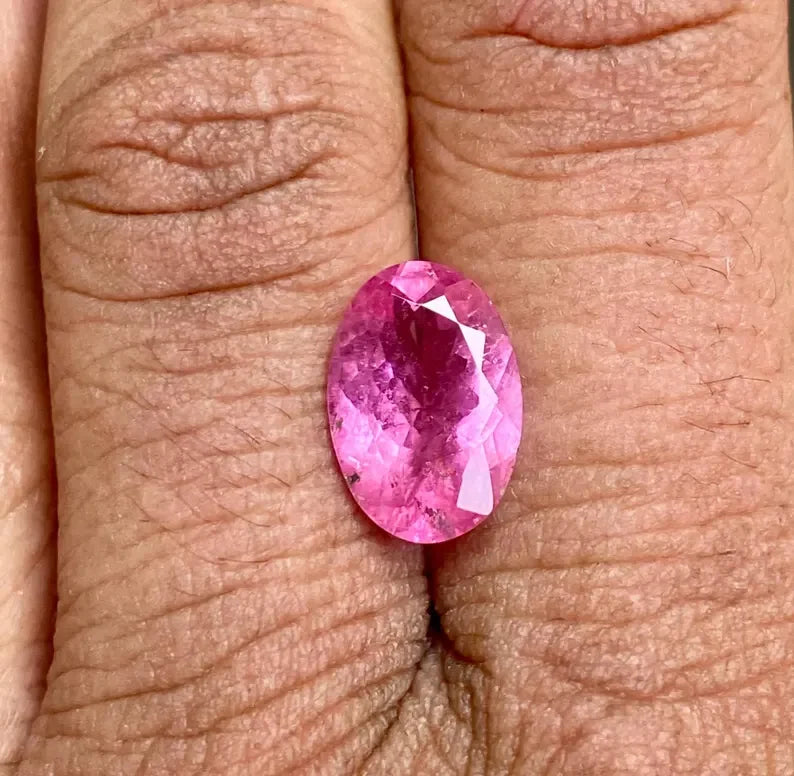 Oval-cut pink sapphire gemstone on fingertip, faceted sparkle visible