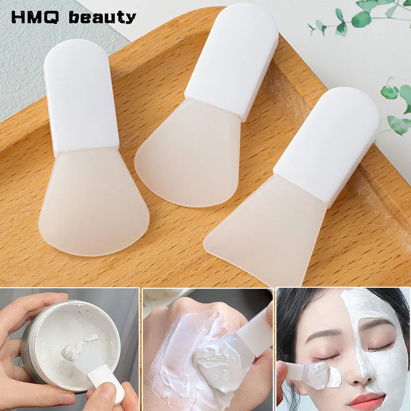 Three white silicone facial mask brushes with flexible, spade-shaped tips for applying mud creams, shown in use.