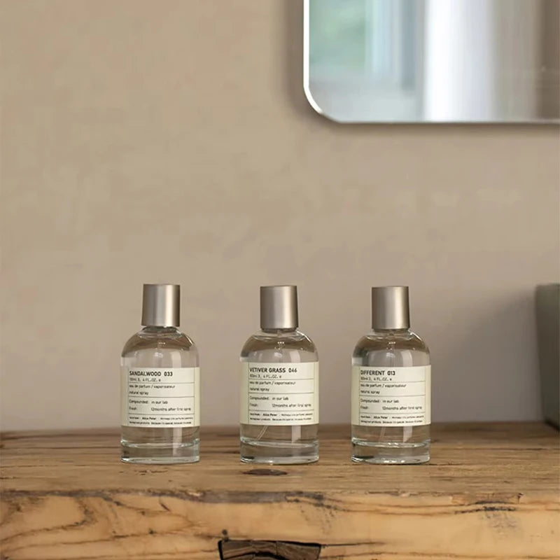 Alice Peter 100ml unisex EDT perfume bottles in sandalwood, vetiver, and bergamot scents on a wooden table.