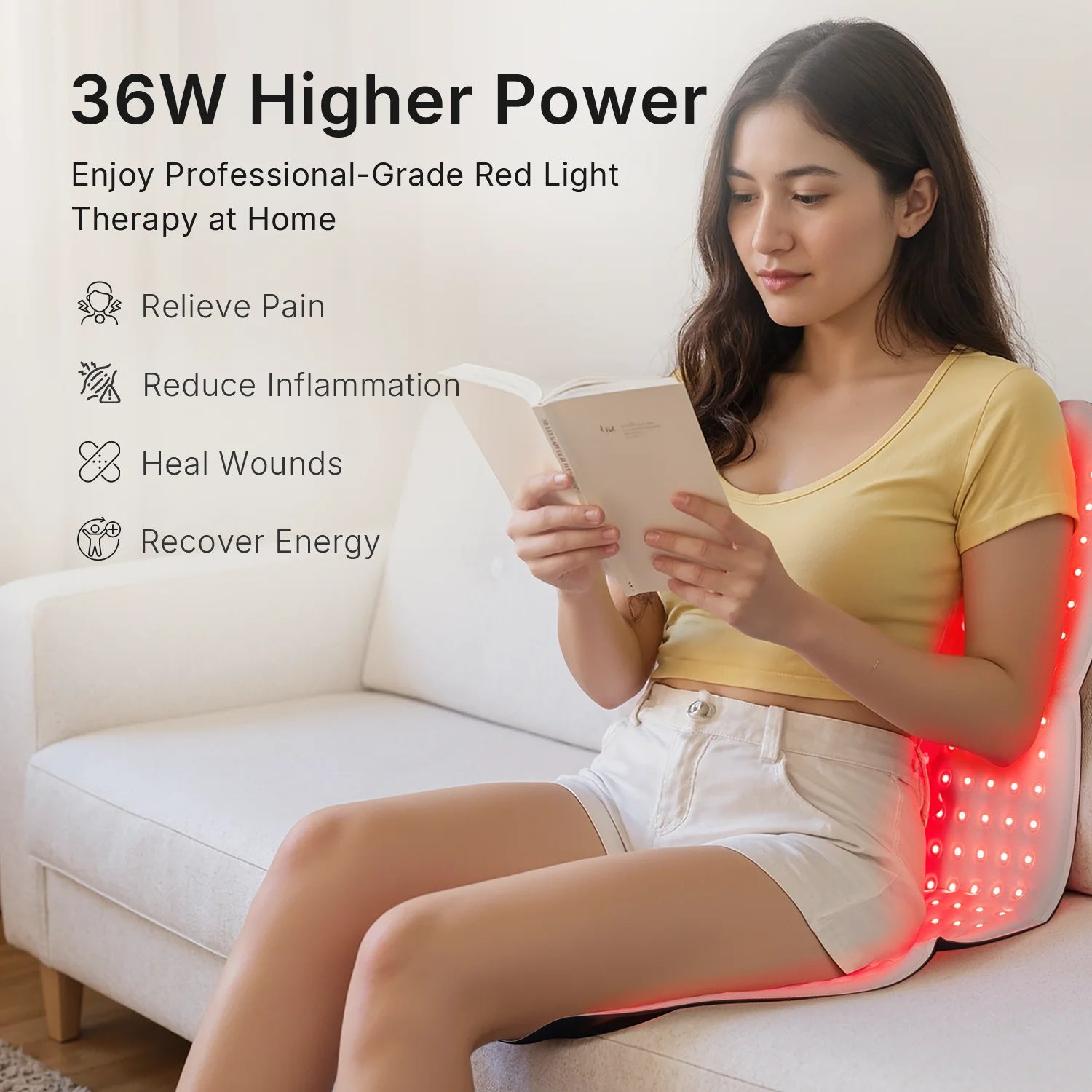 Woman reading on a sofa using a flexible, flat red light therapy mat glowing with bright red LED lights behind her.