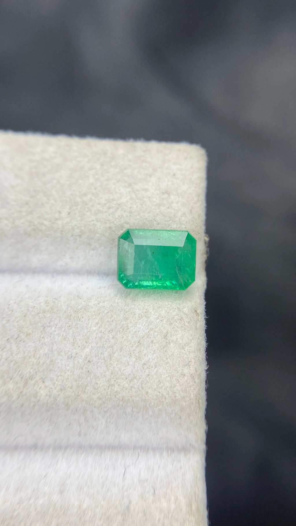 Green emerald-cut octagon loose gemstone resting on white cloth, side perspective