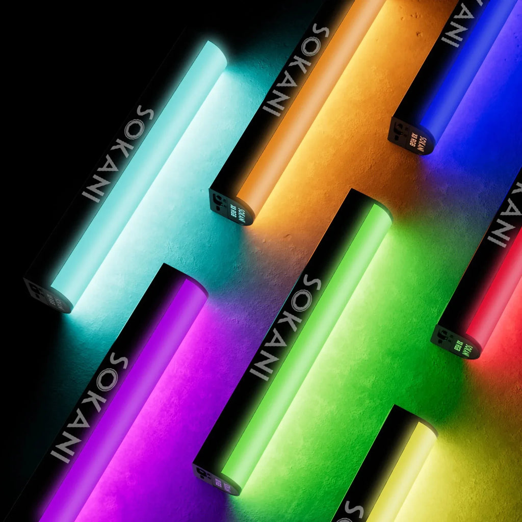 Multiple handheld RGB LED light sticks in various glowing colors arranged on a dark surface for photography lighting.