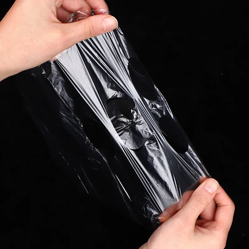 Hands holding a thin, transparent plastic facial mask sheet with pre-cut openings against a black background.