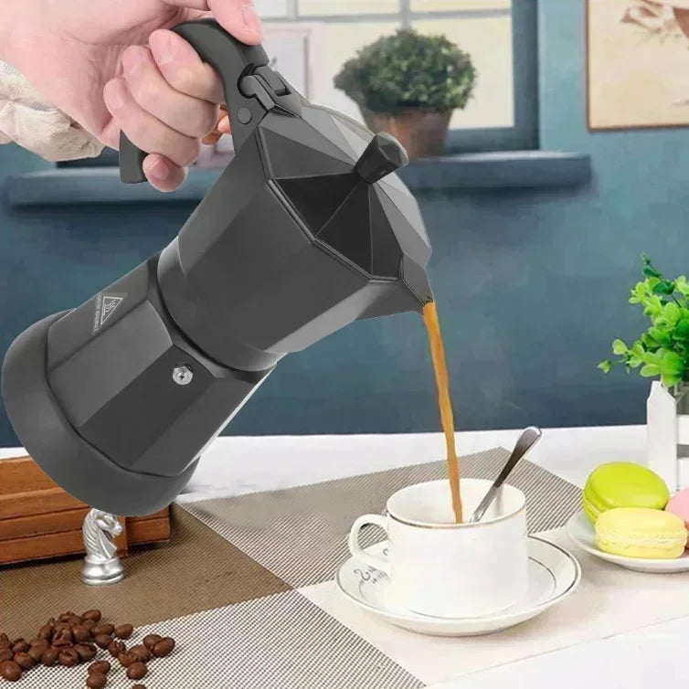 Hand pouring coffee from a matte black aluminum moka pot stovetop espresso maker into a white porcelain cup.