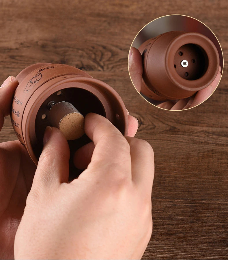 Hands inserting a moxa stick into a brown, ceramic meridian moxibustion cup with engraved markings.
