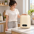Portable washing machine in cream on kitchen counter with a woman holding fresh laundry.